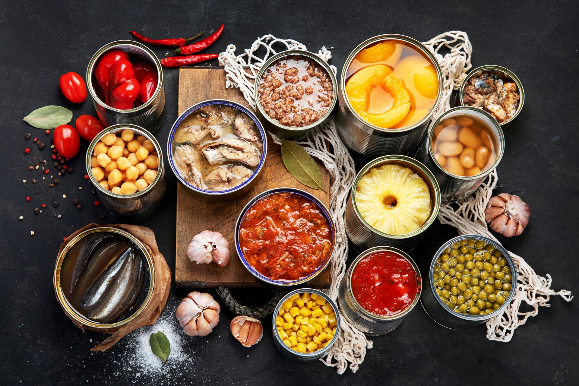Various canned vegetables, meat, fish and fruits in tin cans. On a dark background. Top view.